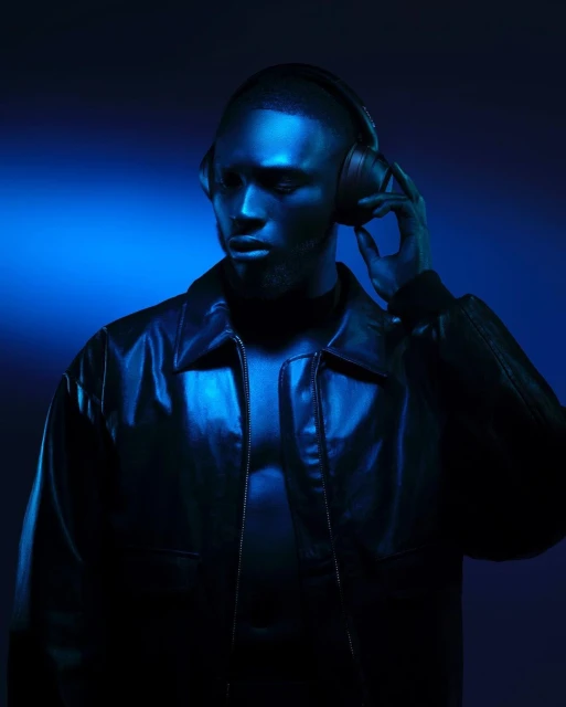 Man wearing headphones and a black leather jacket is featured in a striking portrait with dramatic blue lighting and a dark background.