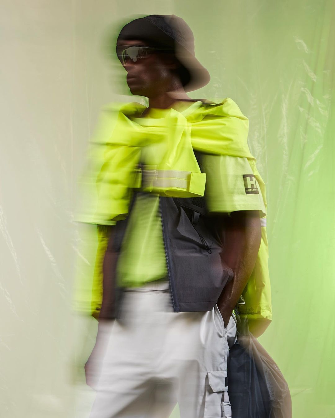Fashionable adult male poses in yellow and grey apparel with a black bucket hat and sunglasses. Shot with motion blur effect.