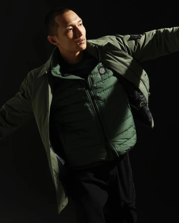 East Asian man wearing a green quilted vest and jacket, captured in dramatic low-key lighting against a dark background.