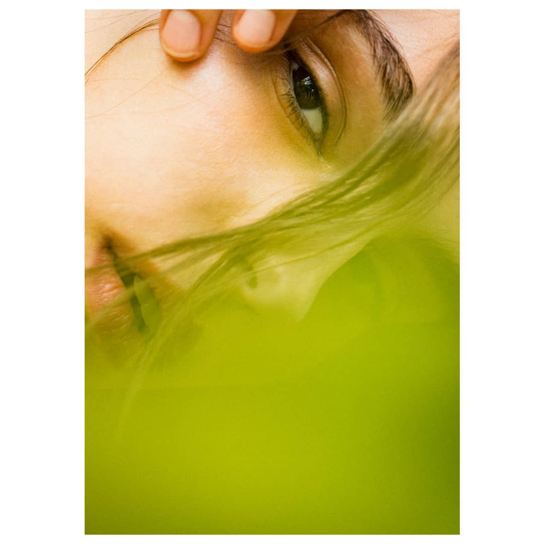 Close-up portrait of an adult woman with her hand on her forehead and windblown hair over a soft green blurred background.