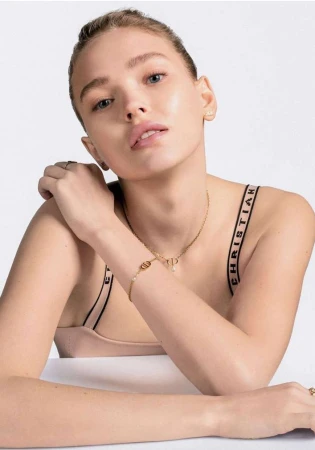 Close-up portrait of a woman wearing gold jewelry and branded strap apparel against a white background