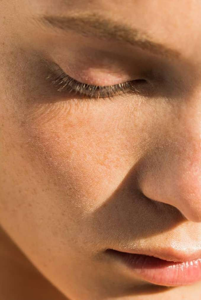 Close-up shot of a person's face with a closed eye, capturing the details of the eyelashes, skin texture, and subtle lighting.