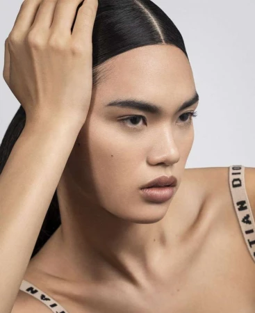 Close up beauty portrait of a woman with slicked dark hair posing against a neutral background by Maeva Delacroix
