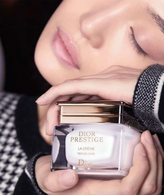 Dior Prestige cream product shot with a woman's face and hands holding the product in a beauty and fashion editorial setting.
