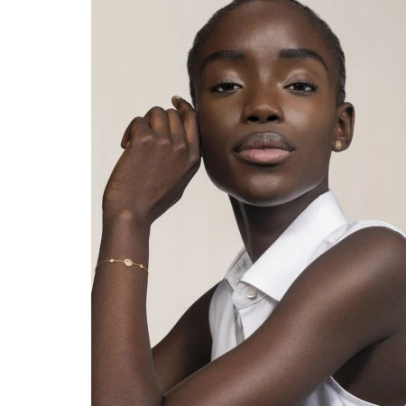Close-up portrait of a black woman wearing a white collared shirt, gold earrings, and a delicate gold bracelet by Maeva Delacroix
