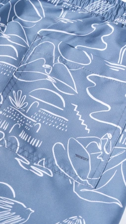 Close-up on blue swim trunks featuring a white line art pattern with tropical island, beach, and ocean motifs in a repeating design.