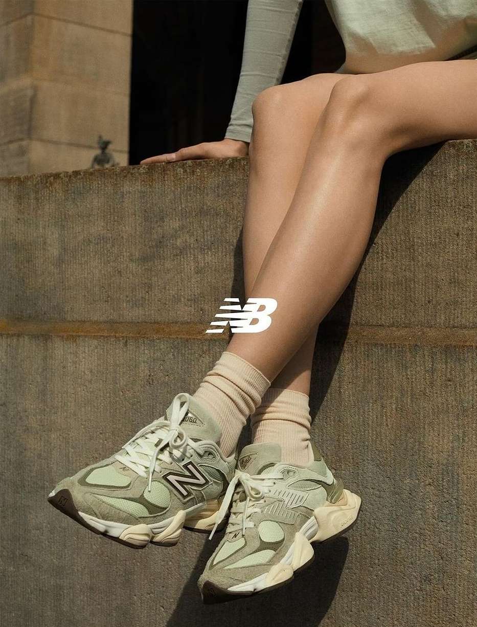 Athletic shoes: A woman sits with gray New Balance sneakers. Neutral-toned socks and background. Product, shoe, and fashion photography.
