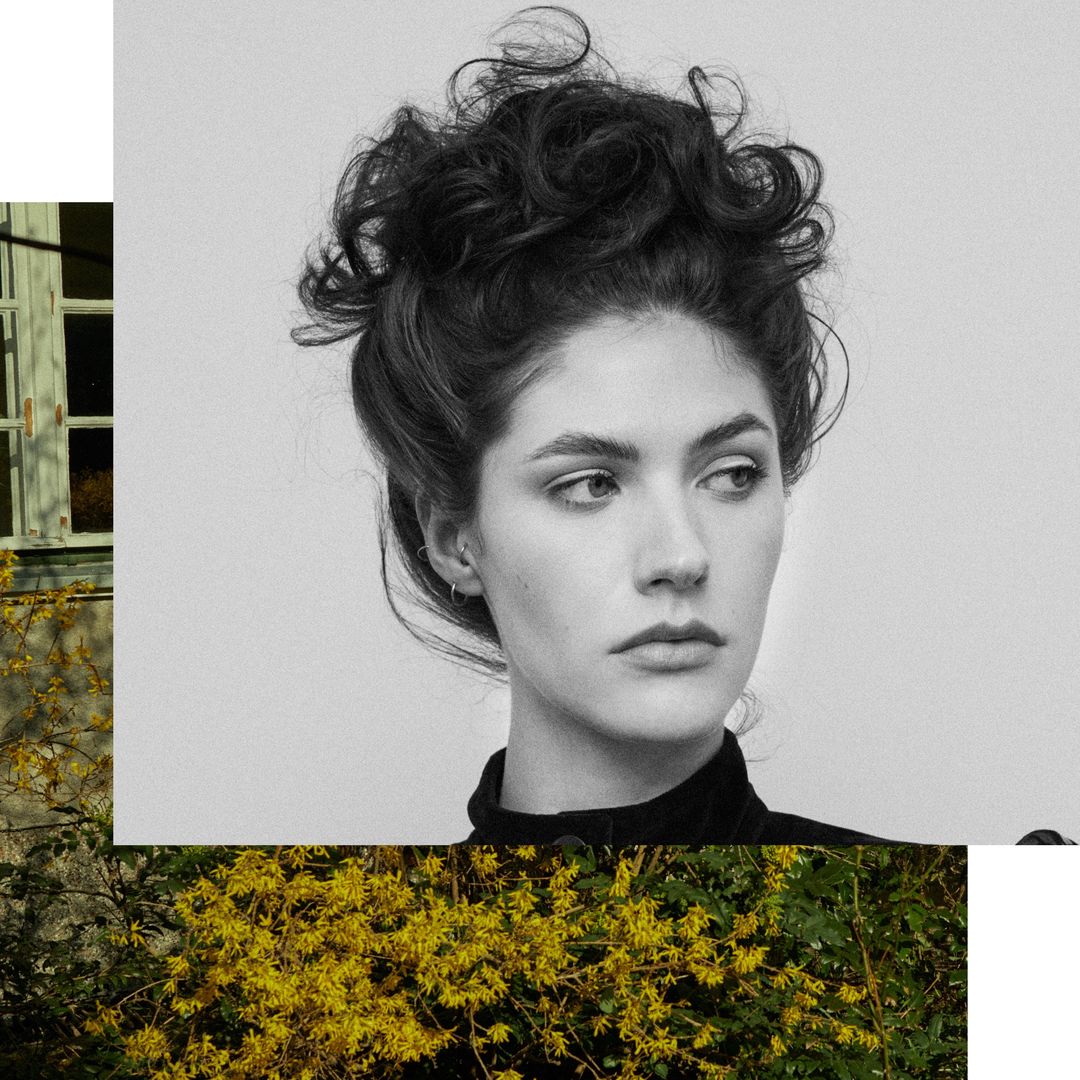 Monochrome portrait of a woman with dark curly updo hair in a black top against a collage background.