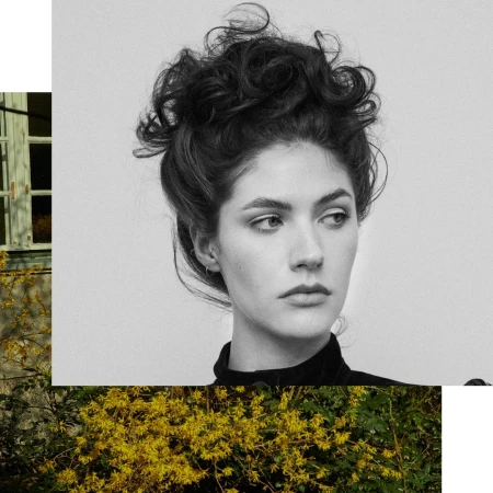 Monochrome portrait of a woman with dark curly updo hair in a black top against a collage background.
