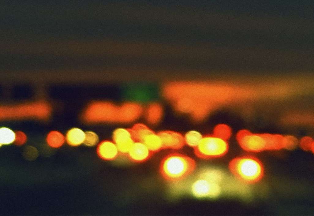 Blurred night scene with illuminated city lights and traffic lights, creating a bokeh effect against a dark sky.