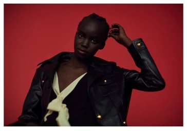 Black woman wearing a black leather jacket and yellow scarf against a red background by photographer Magnus Magnusson