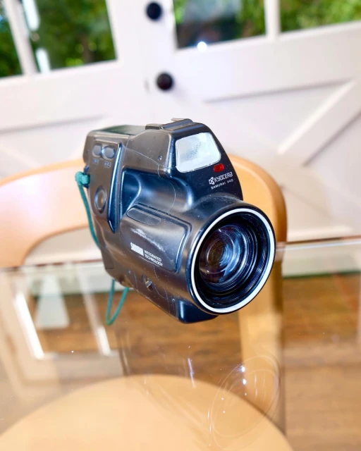 Vintage Kyocera Samurai movie camera on a glass table, showcasing its black exterior and unique design with a blurred background. 