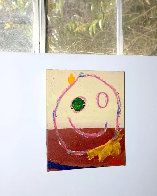 Whimsical child's art: a painted canvas features a colorful smiley face, creating a cheerful, naive aesthetic, hung near a window.