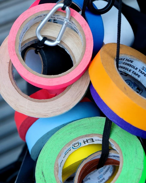 Close-up of colorful rolls of console tape hanging from a black cord with a carabiner clip, creating an abstract artistic display.