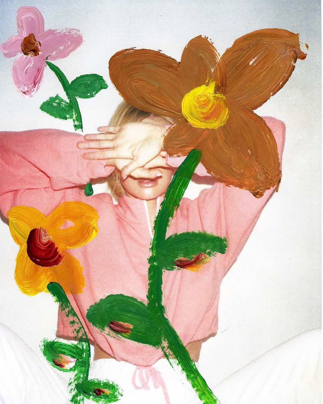 Artistic portrait of a young woman partially obscured by painted flowers in pink and brown hues, covering her eyes with her hands.