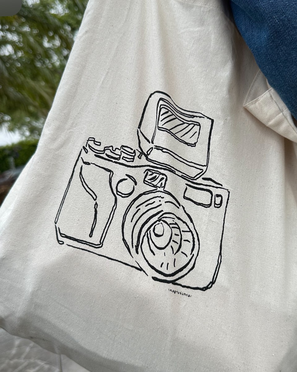 Drawing of a camera on a tote bag, showing the lens, flash, and body, capturing a blend of fashion and photographic themes.