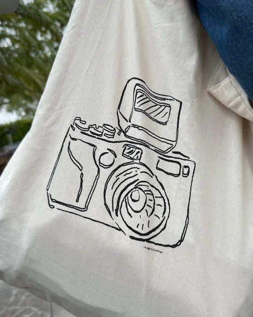 Drawing of a camera on a tote bag, showing the lens, flash, and body, capturing a blend of fashion and photographic themes.