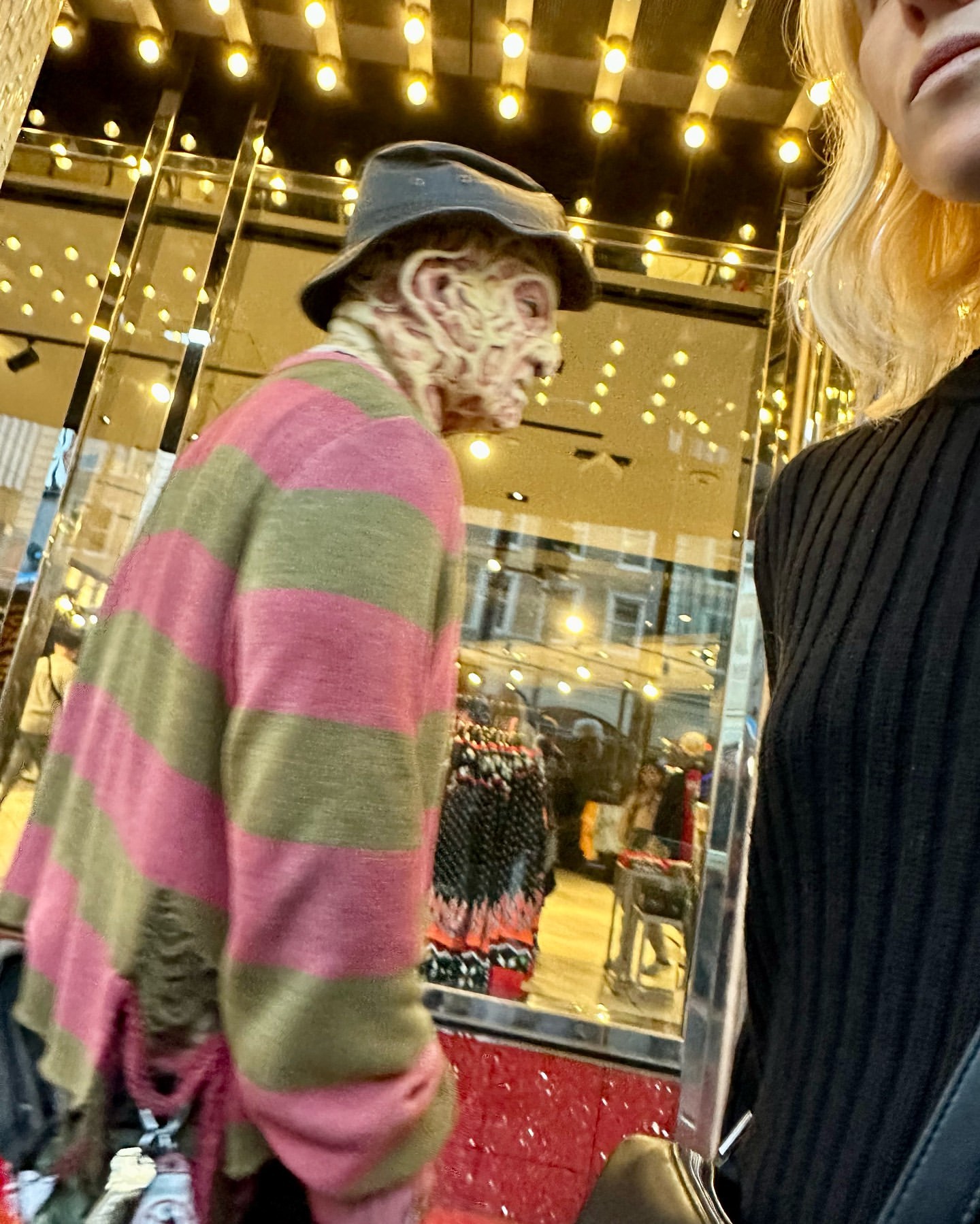 Mannequin dressed as Freddy Krueger, with a striped sweater and hat, is displayed in a store window near a person in black.