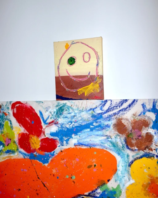 Colorful abstract art featuring painted and drawn elements, including a child-like face, set against a clean white backdrop.