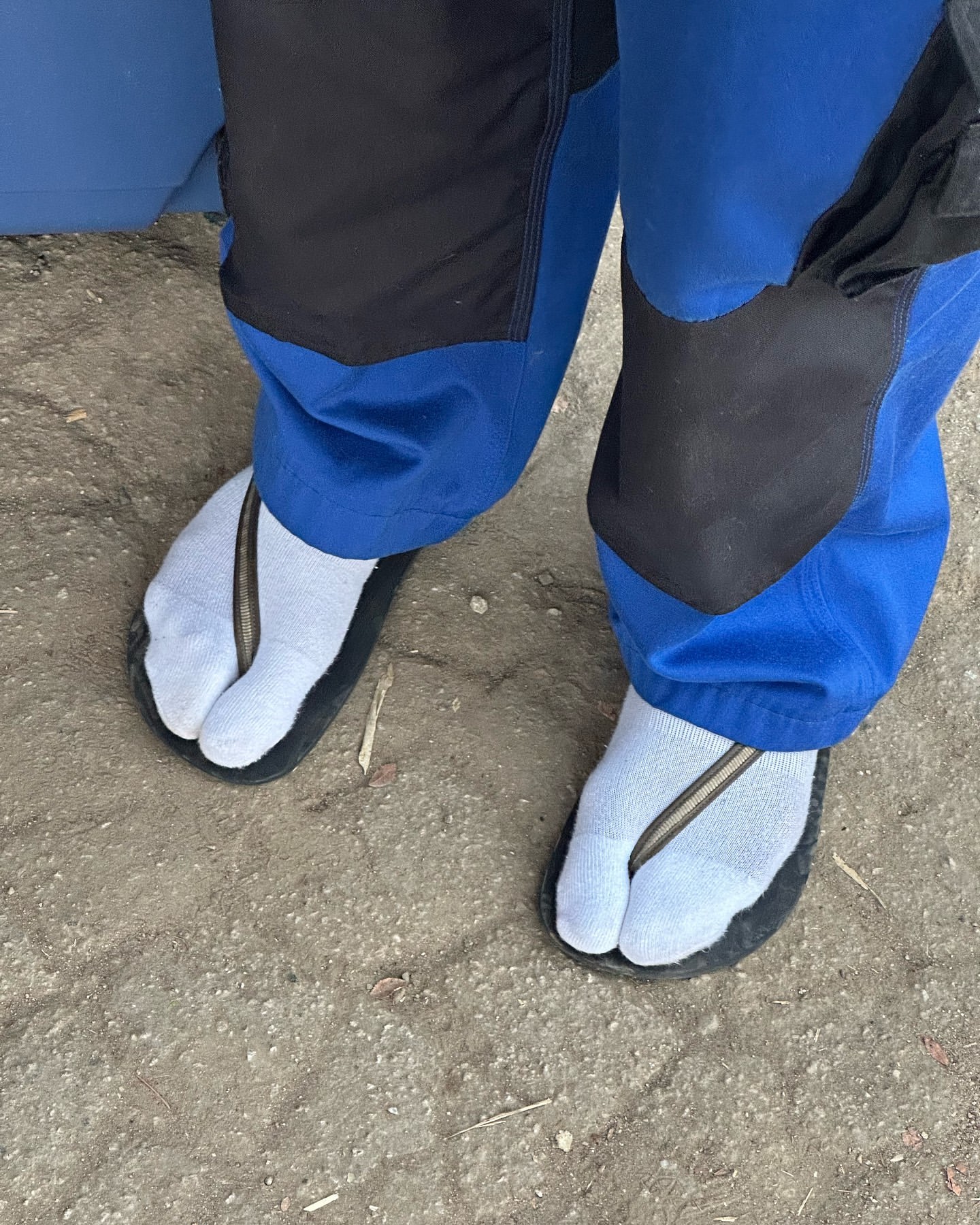 Person wearing light blue socks with black toe-strap sandals standing on neutral ground, capturing a distinct sense of casual footwear.