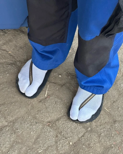 Person wearing light blue socks with black toe-strap sandals standing on neutral ground, capturing a distinct sense of casual footwear.