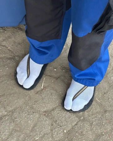 Person wearing light blue socks with black toe-strap sandals standing on neutral ground, capturing a distinct sense of casual footwear.