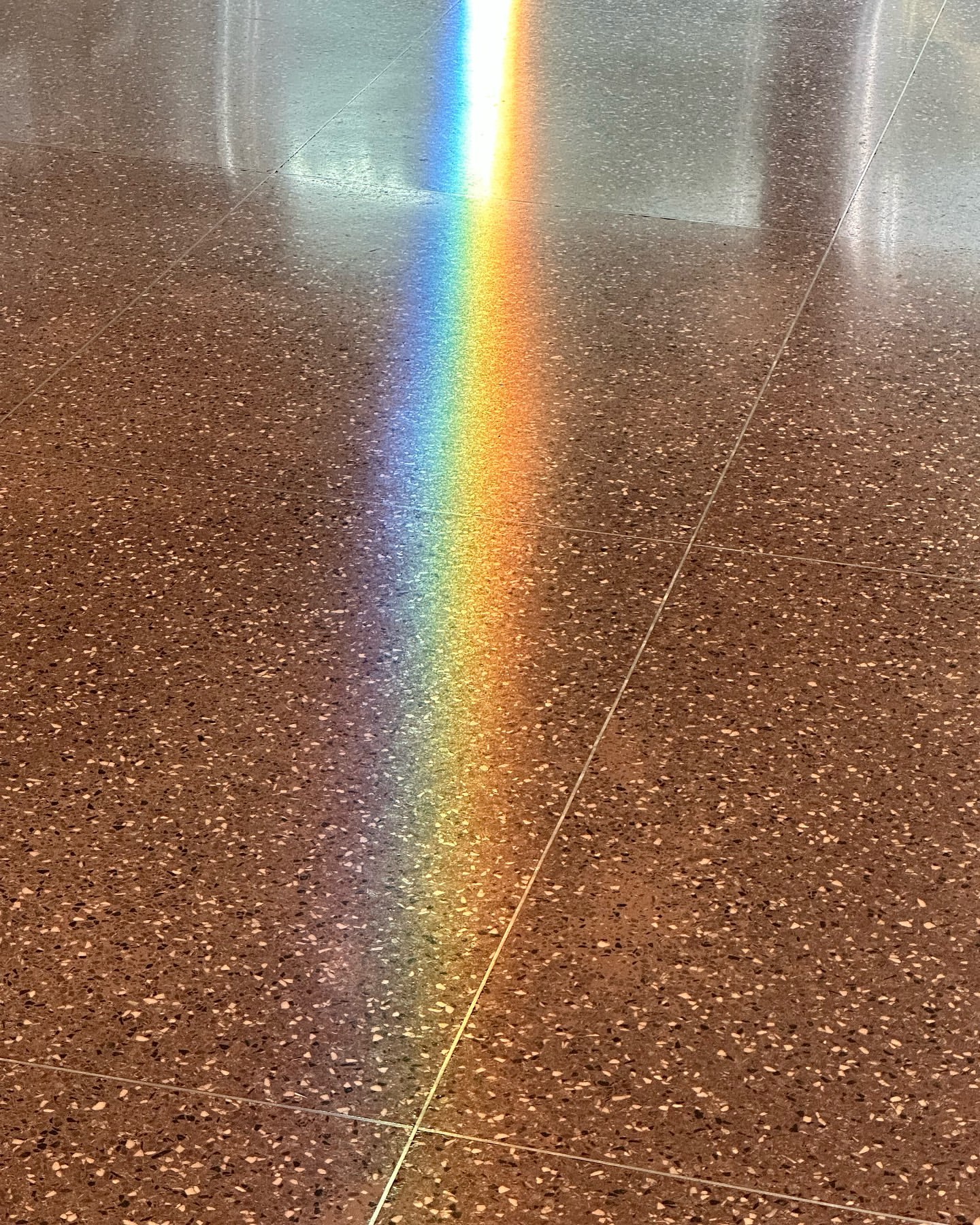 A vibrant rainbow light shines on a speckled tile floor, creating a spectrum of colors against the neutral background.