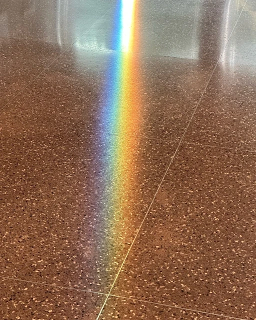 A vibrant rainbow light shines on a speckled tile floor, creating a spectrum of colors against the neutral background.