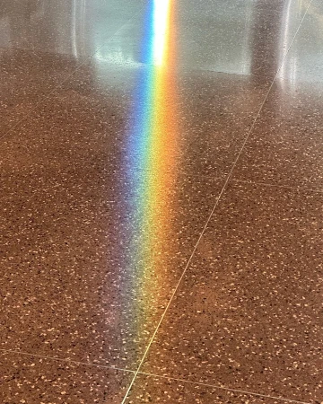 A vibrant rainbow light shines on a speckled tile floor, creating a spectrum of colors against the neutral background.