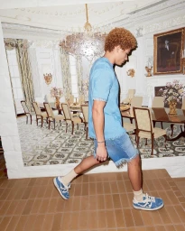 Young man with curly brown hair walking in profile against a backdrop depicting a formal dining room
