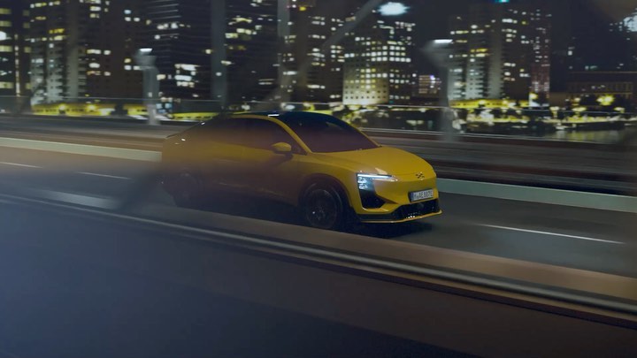 Yellow electric car drives on a bridge at night with city lights in background. Automotive shot with long exposure, vehicle in motion.