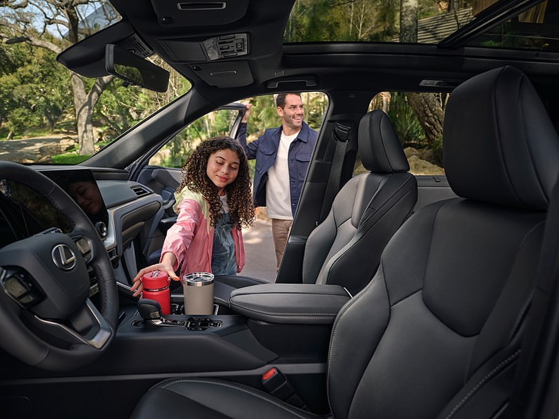 Father and daughter standing outside the interior of a Lexus SUV. The young girl holds two beverage containers.