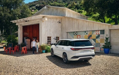 White SUV parked on a gravel yard in front of a rustic wooden barn with a man and woman walking nearby.