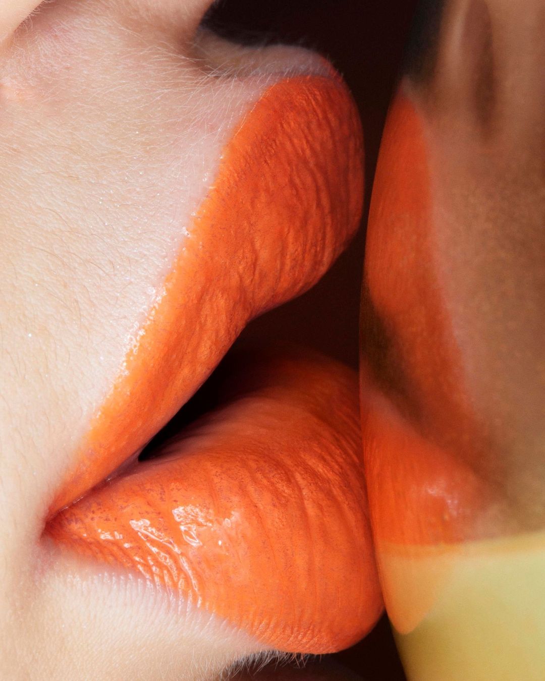 Close-up shot of a woman's lips painted with vibrant orange lipstick, creating a glossy, bold, and eye-catching makeup look.