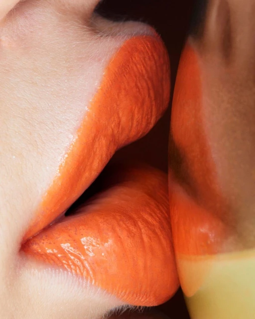 Close-up shot of a woman's lips painted with vibrant orange lipstick, creating a glossy, bold, and eye-catching makeup look.