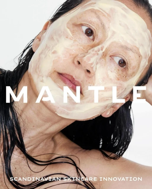 Close-up beauty shot of an adult woman with a facial mask on her face, damp black hair, bare shoulders, against a white background.