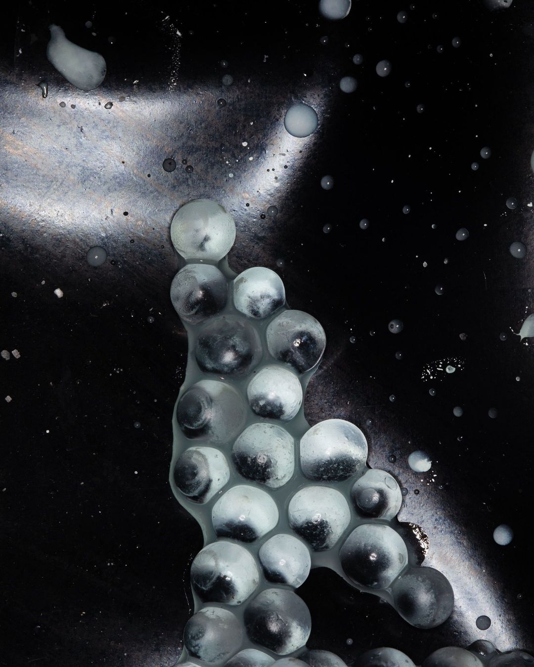 Abstract image featuring clusters of translucent spheres against a dark, textured backdrop with scattered highlights and reflections.