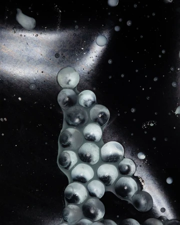Abstract image featuring clusters of translucent spheres against a dark, textured backdrop with scattered highlights and reflections.