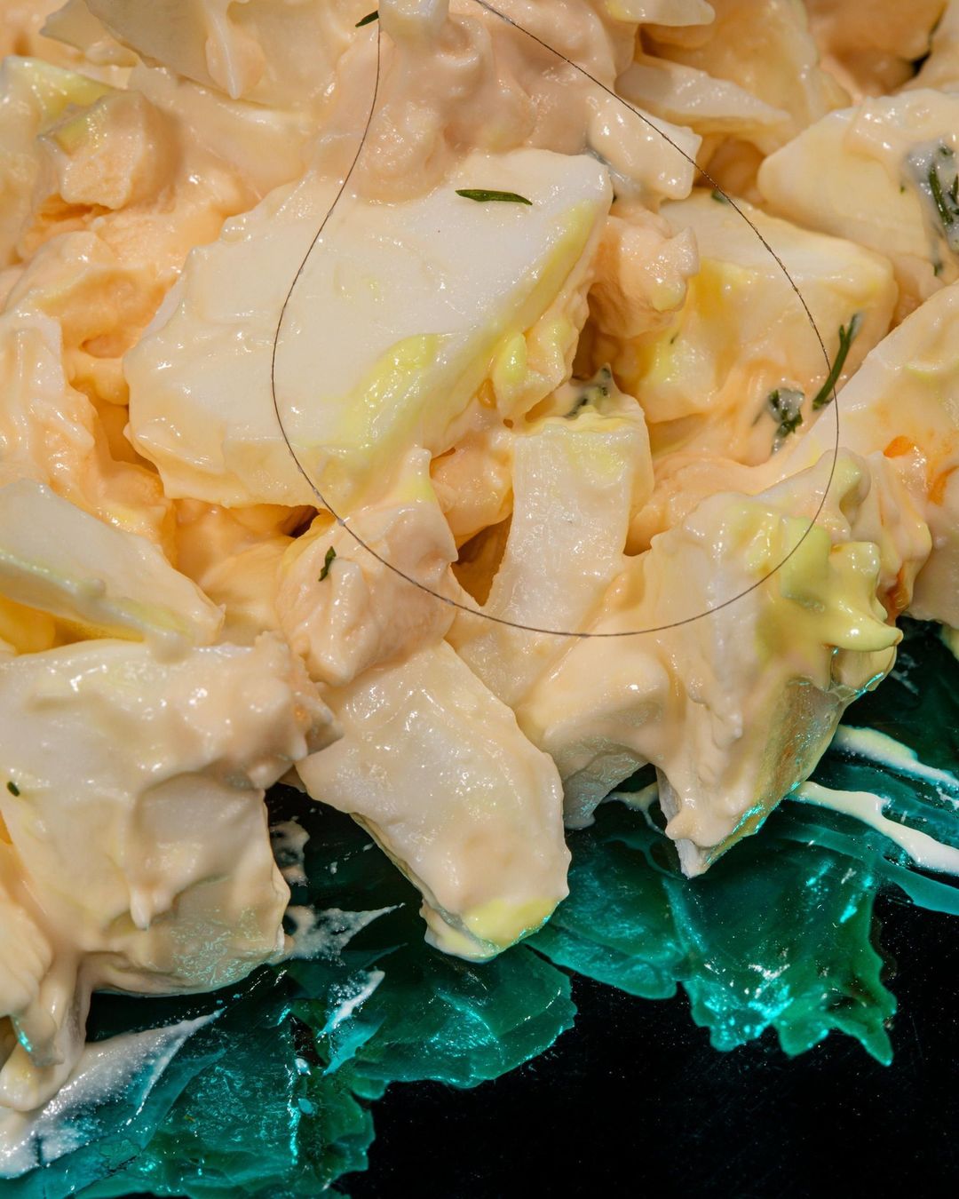 Close-up of creamy egg salad with green garnish on a dark surface. Dominant colors are light beige, white, and green.