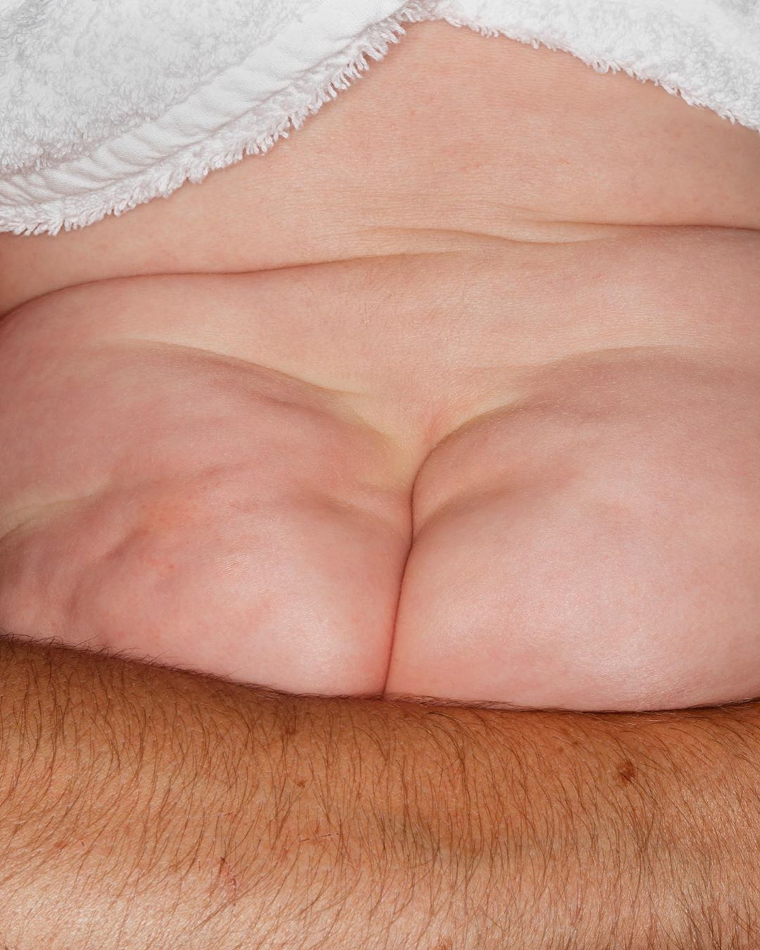 Close-up shot of a person lying down with the lower back and top of the legs exposed, covered partially by a white towel.