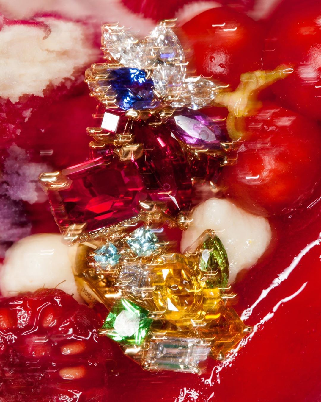 Macro shot of gold jewelry adorned with colorful gemstones. Red and pink berry background.