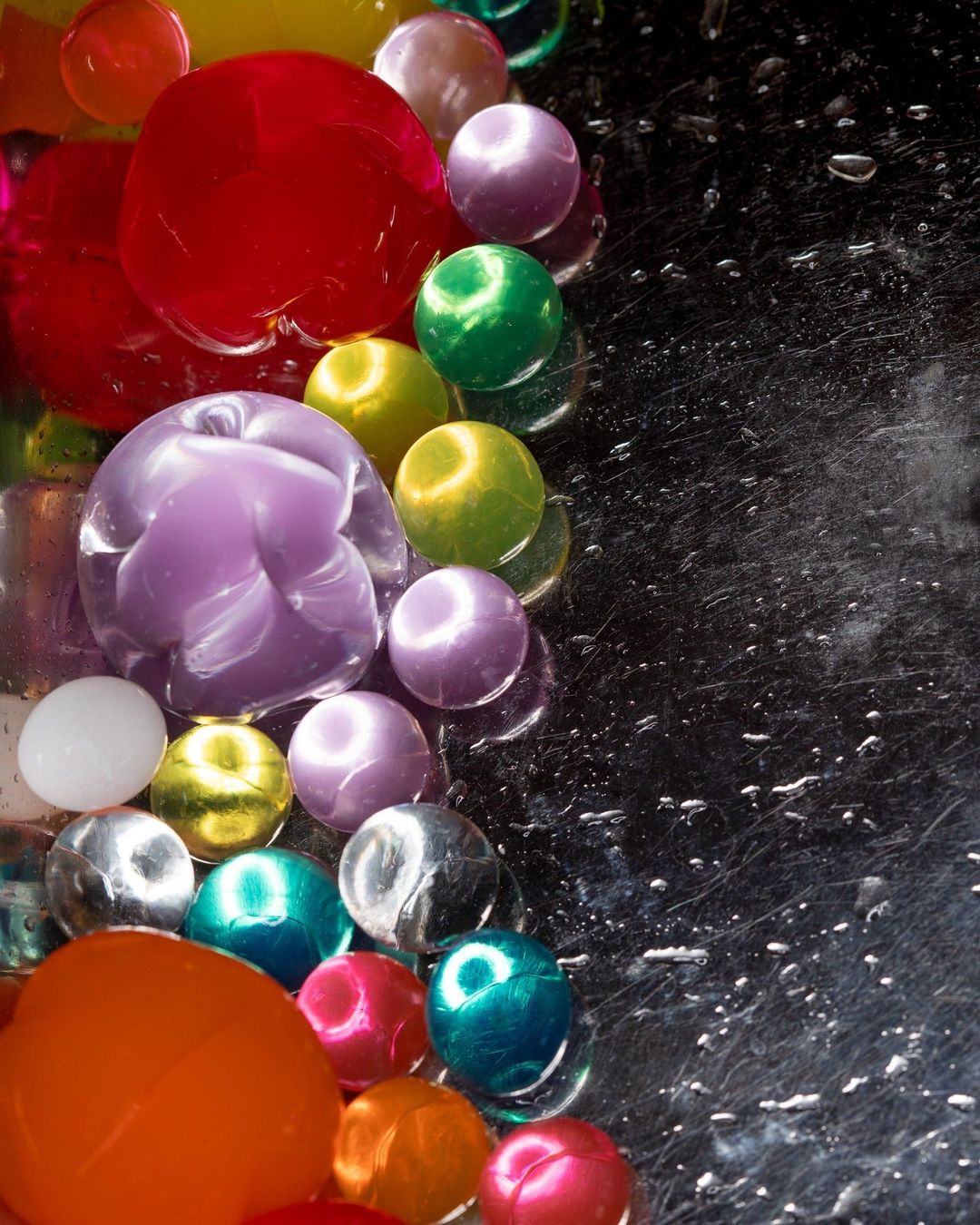 Macro abstract still life of transparent colorful marbles in red, purple, green, yellow, orange and black on a shiny reflective surface.