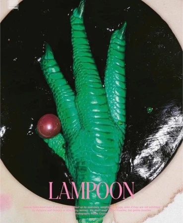 Abstract studio shot of a green painted chicken foot with a red orb set against a black backdrop and off-white foreground.