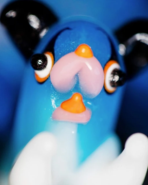 Close-up of a blue cartoon-like cat figurine with large, black ears, a pink nose, and white paws in a softly blurred composition.