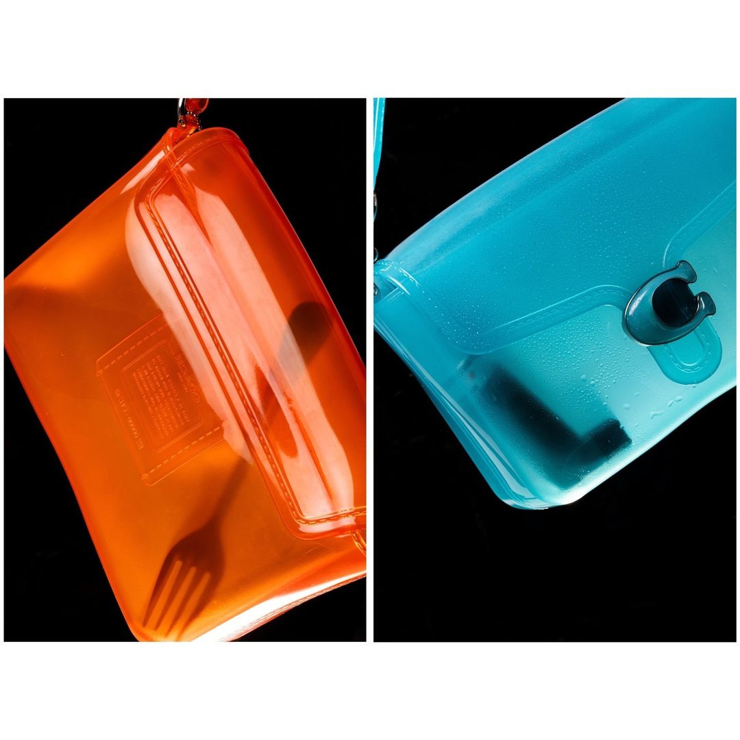 Orange and blue translucent clutch purses with a fork inside, presented against a stark black background, with a hanging loop.