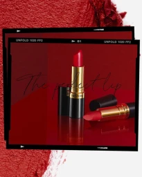 Close-up product photography of a red lipstick tube standing upright with a second lipstick lying beside it on a glossy red reflective surface.
