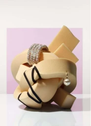 Sculptural tan foam knot with sparkling diamond cuff and pearl earring by Makerie Studio against a pink and white background.