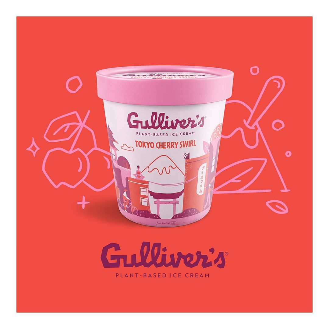 Close-up of a container of plant-based ice cream by Gulliver's, featuring a Tokyo Cherry Swirl flavor, set on a coral-colored surface.