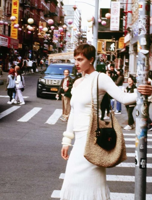 Woman in a white outfit posing on a city street in Chinatown, New York, with colorful lanterns and street signs creating a lively atmosphere.