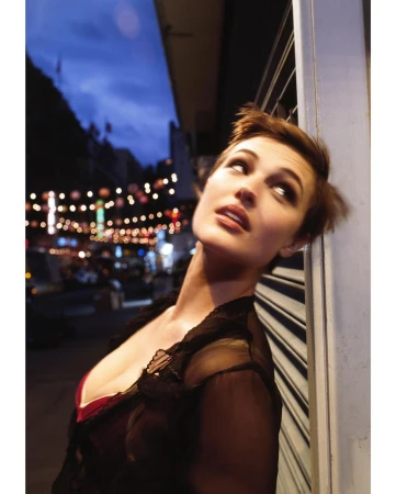 Close-up portrait of a woman with short brown hair leaning against a metal shutter in London at dusk.